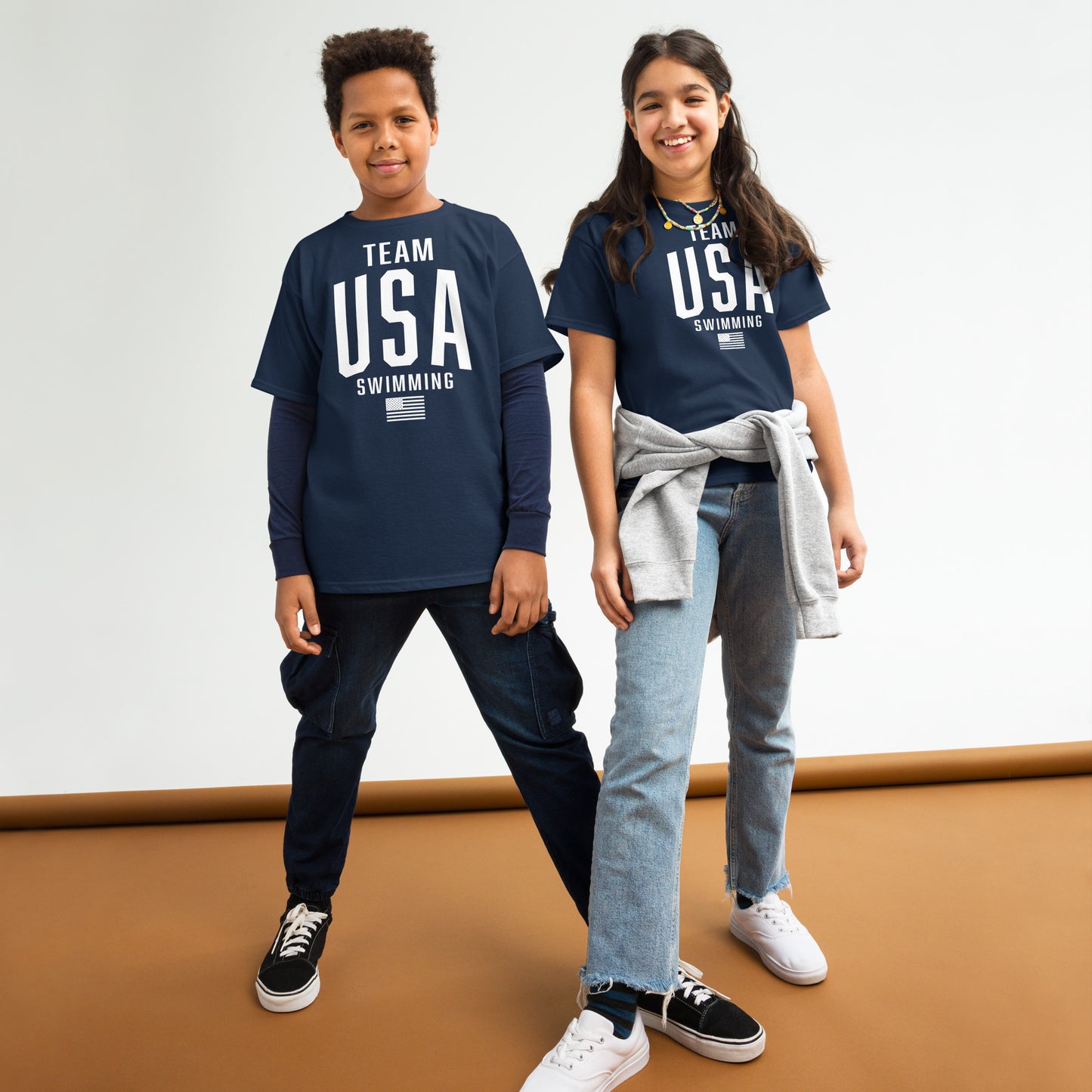 Two kids wearing navy Team USA Swimming Patriotic Youth T-Shirts by TrendySwimmer, styled casually for active youth apparel.