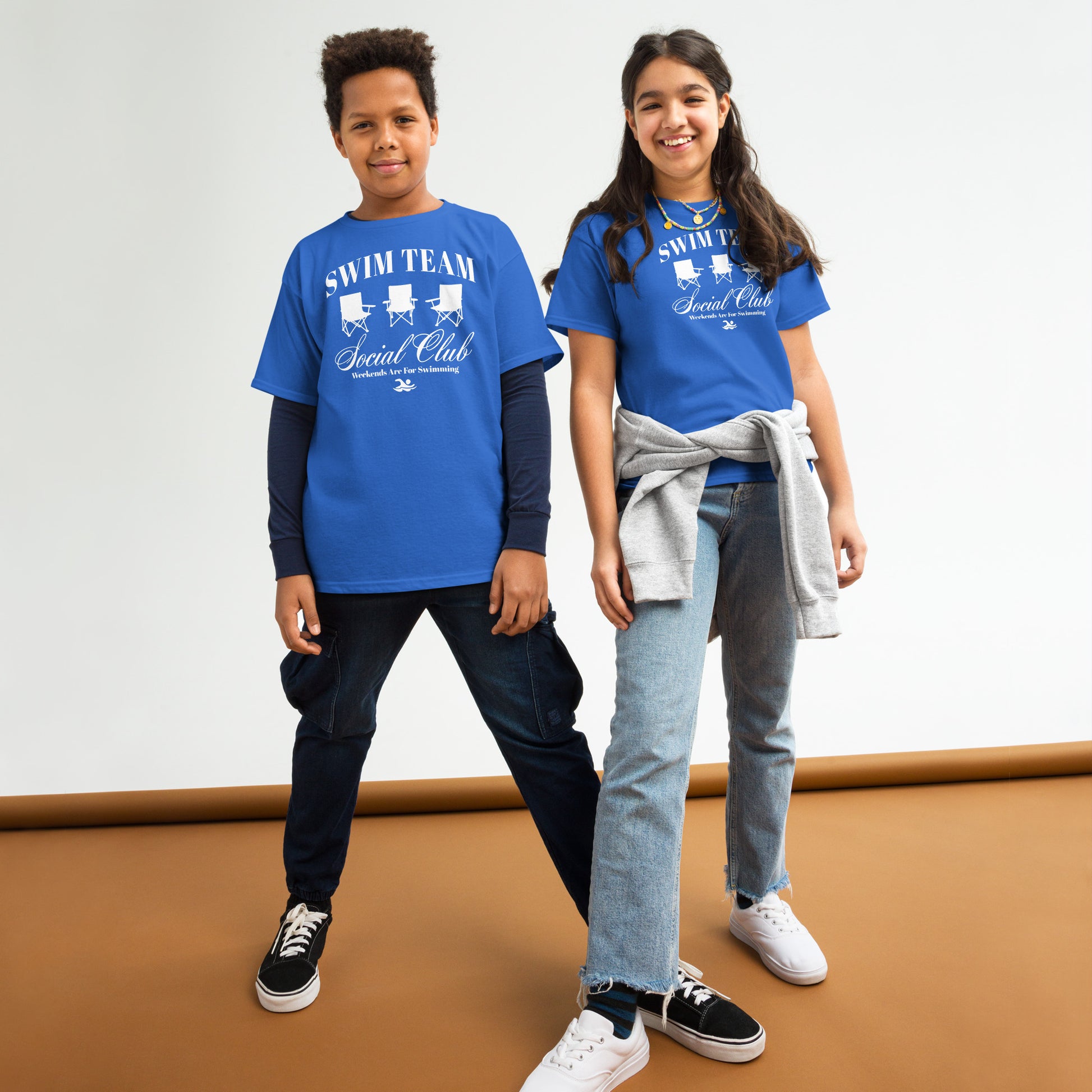 Two kids wearing royal blue Swim Team Social Club Youth T-shirts by TrendySwimmer, styled casually with jeans and sneakers.