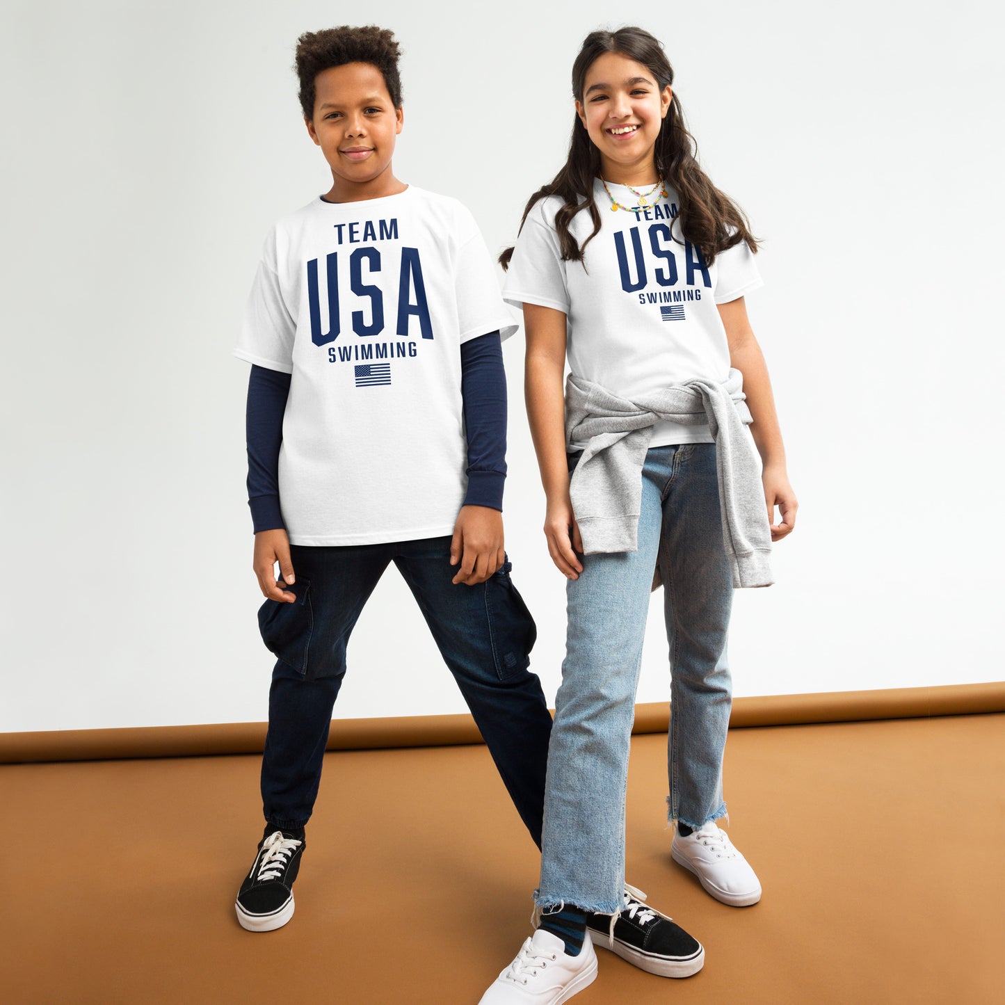 Two kids wearing Team USA Swimming Patriotic Youth T-Shirts in white, styled casually. Ideal for young swimmers showing national pride.